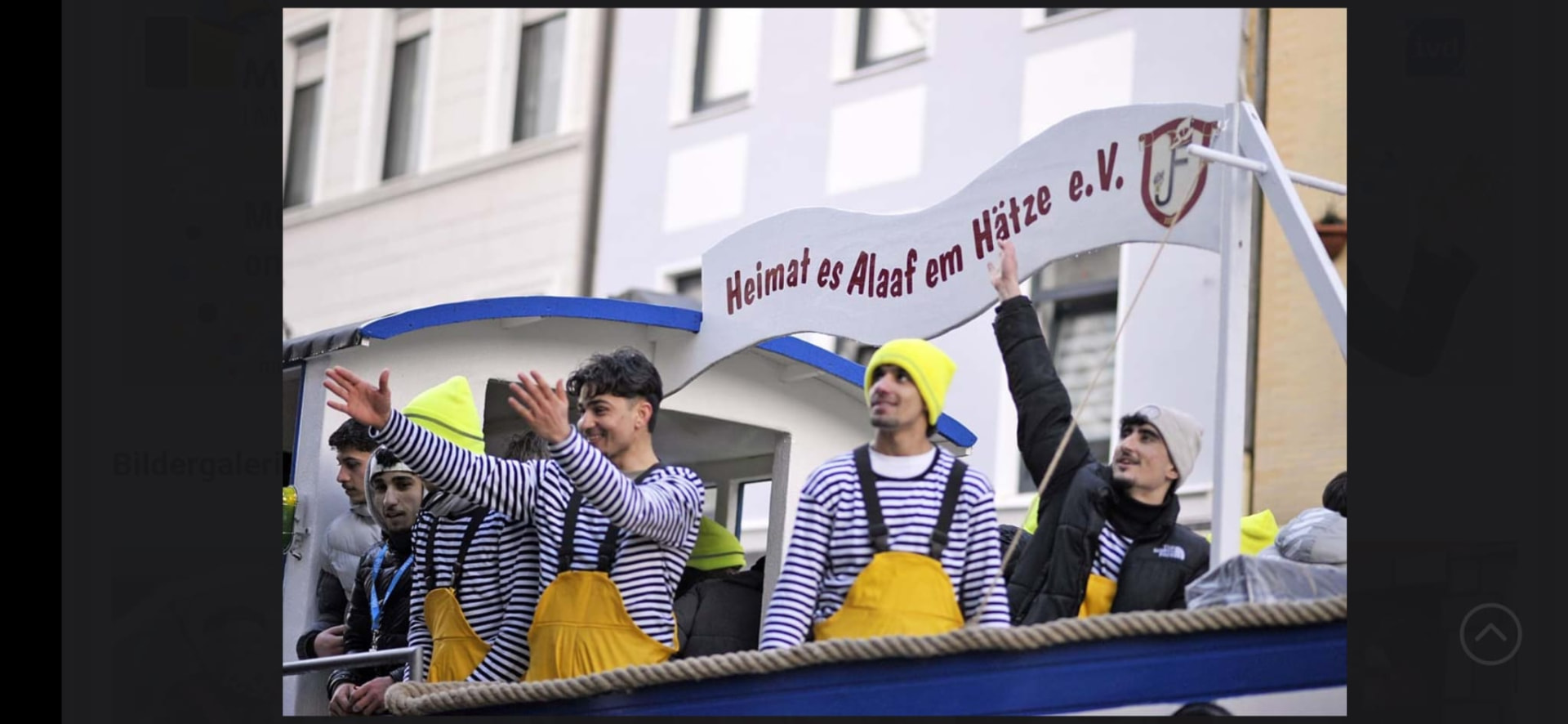 Junge Männer auf einem Karnevalswagen winken dem Publikum zu