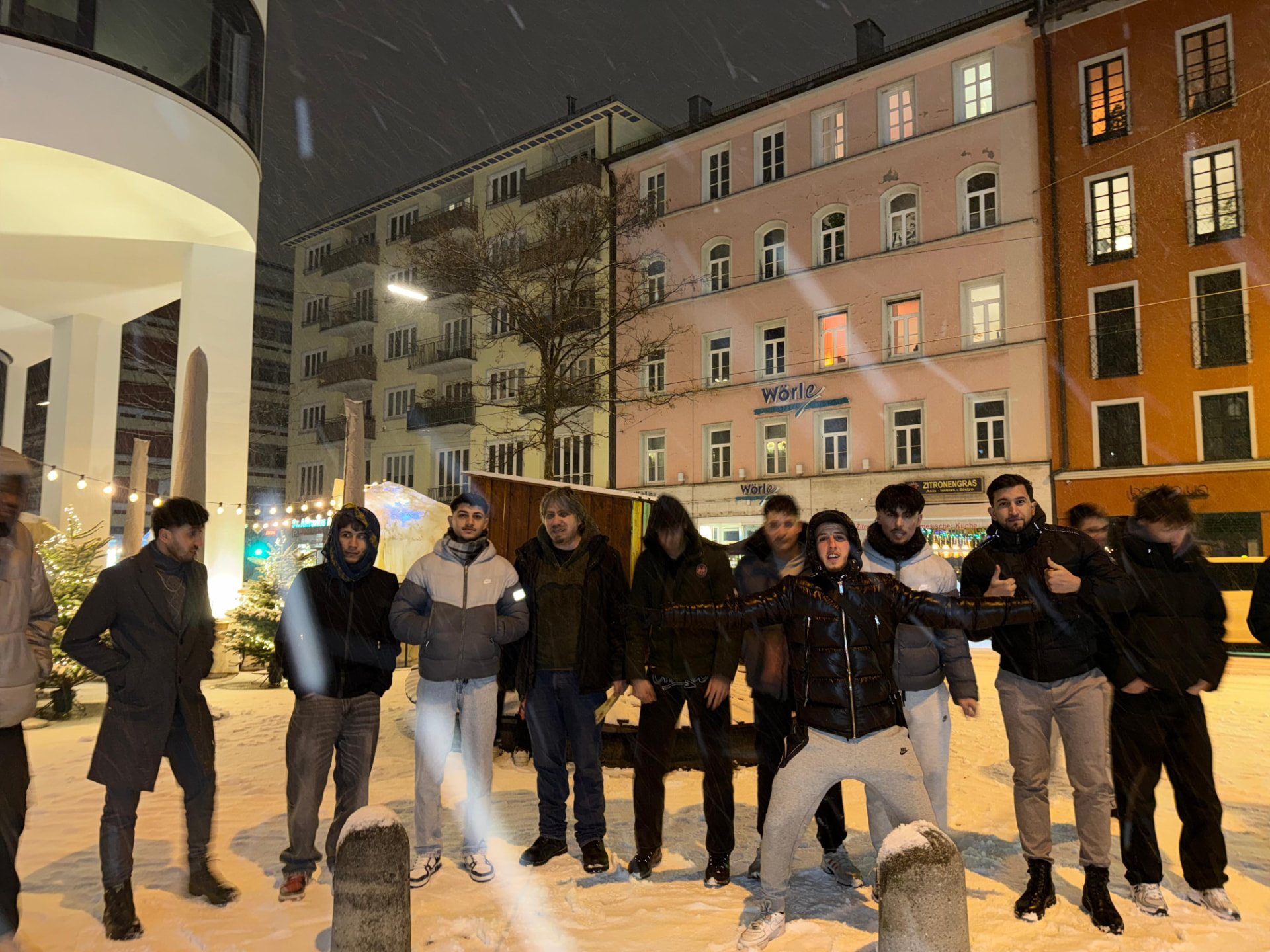 Gruppe junger Menschen bei Schneefall abends auf einem Platz